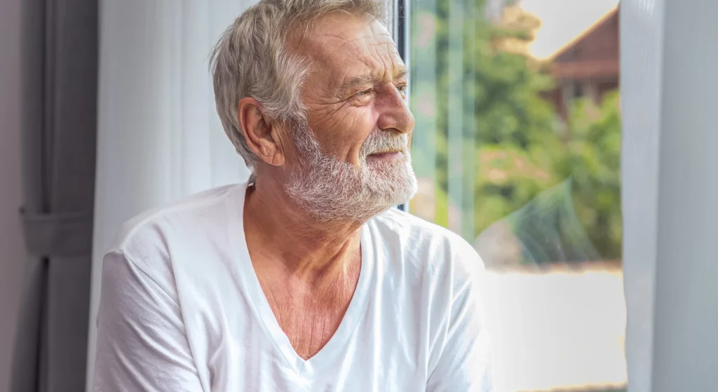An older man smiling by a bright window
